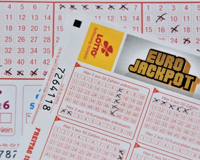 Three lottery tickets are displayed, including Eurojackpot and Super 6. Various numbers are marked on the tickets, with some crossed out and others checked. The Eurojackpot ticket is partially visible with the logo prominently displayed, and a ticket number is visible on one of the tickets.